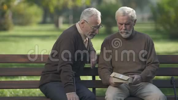 两个男朋友在公园的长椅上看着照片微笑着旧时记忆视频的预览图