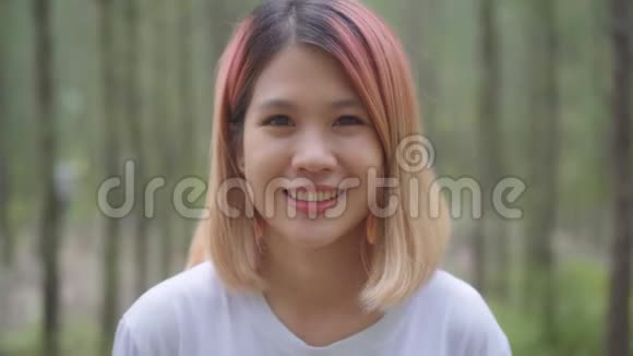 健康美丽的年轻亚洲跑步女子在森林里跑步后感到快乐的微笑和寻找相机视频的预览图