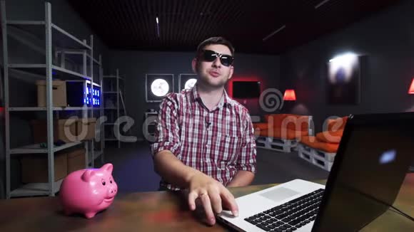 漂亮的男士戴着太阳镜对着镜头说话有猪和笔记本电脑视频的预览图