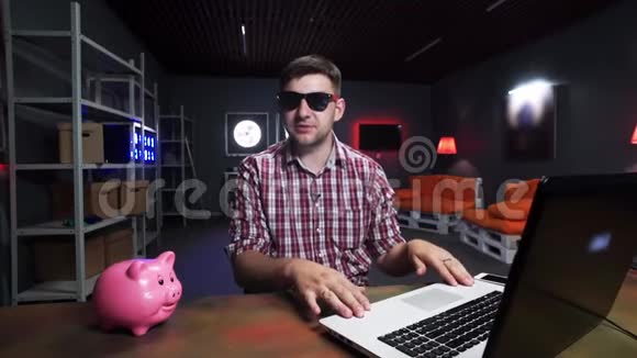 热情的戴墨镜的人在镜头前讲话桌子上有猪和笔记本电脑视频的预览图
