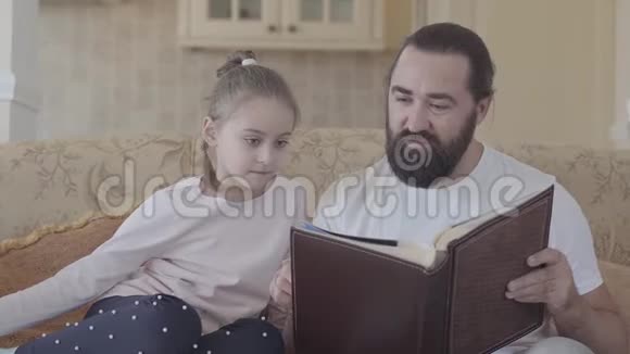 女儿和父亲坐在客厅里看着相册的画像里面有美好的回忆和有趣的故事视频的预览图
