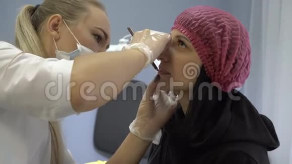 女性美容师在美容院做永久化妆唇年轻女孩用嘴唇的边界包围嘴唇视频的预览图