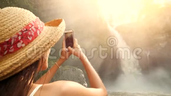 戴草帽的年轻微笑的旅游女孩用手机拍下了惊人的特根南瀑布自然生活方式视频的预览图