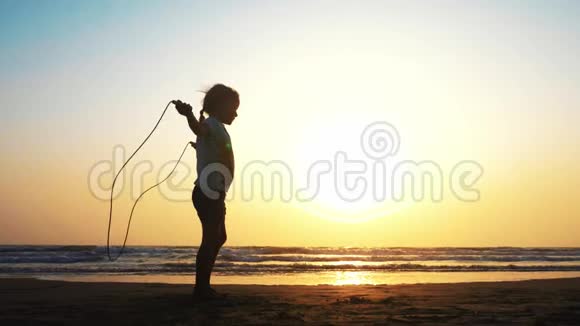 日落时小女孩正在海沙滩上跳着绳子视频的预览图