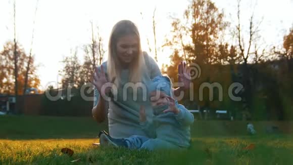 日落时分年轻的妈妈带着一个婴儿在秋天的公园里玩耍在镜头里看视频的预览图