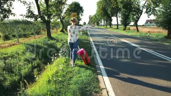 旅行者女孩搭便车在阳光明媚的道路上行走视频的预览图