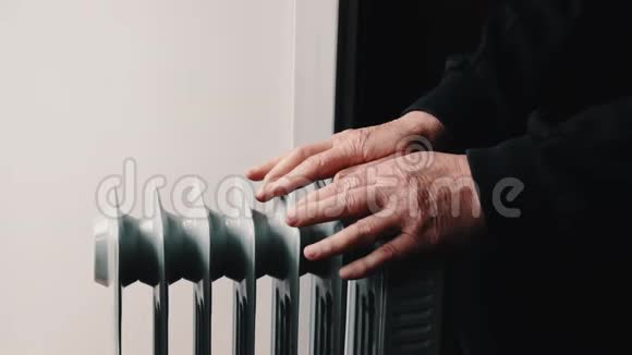 一位年长的老人把手暖和在一个电暖器上视频的预览图