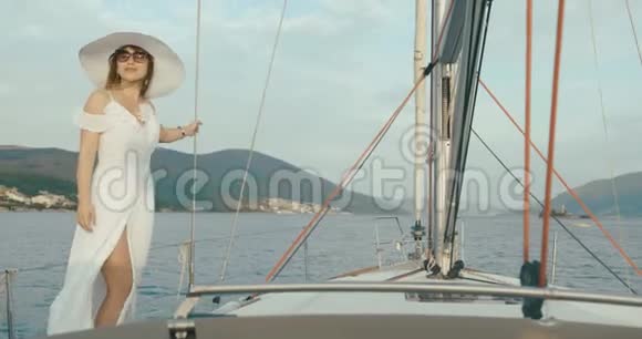 在游艇上的女士一个穿着白色长裙戴着大帽子的女人站在船上在一个多风的天气里骑过湖面视频的预览图
