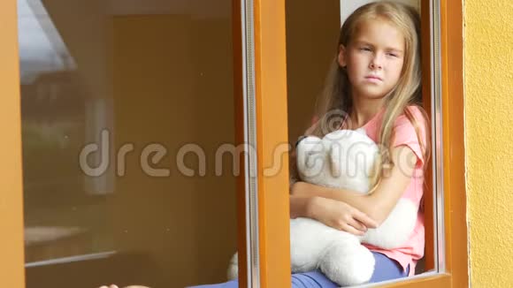 伤心的小女孩抱着一个柔软的玩具坐在窗台上视频的预览图