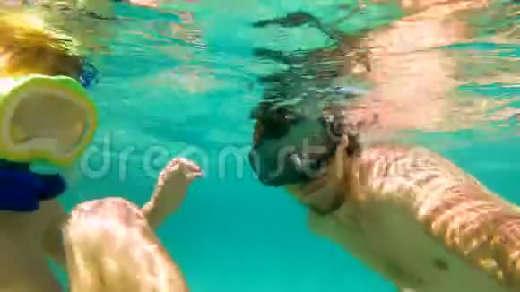 4k水下射击一个可爱的小男孩和他的父亲带着面具和管子在热带海洋里浮潜视频的预览图