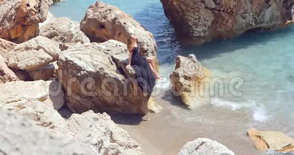 年轻漂亮的女人穿着黑色剪裁优雅的裙子坐在海边视频的预览图