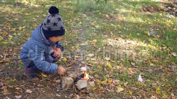 一个快乐的孩子正坐在森林里的炉火旁在一个凉爽的秋日和燃烧的棉花糖旅行烹饪视频的预览图