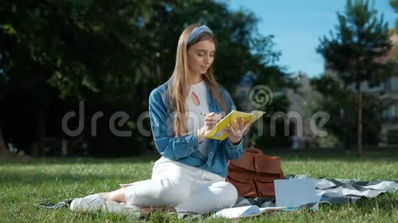 学习笔记的女孩年轻女子坐在公园的草地上拿着一本打开的笔记本远远地看着视频的预览图