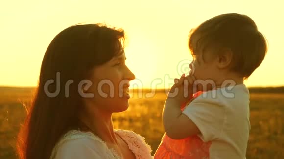 妈妈在和快乐的宝宝说话宝宝坐在妈妈的怀里夕阳下的金色慢动作视频的预览图