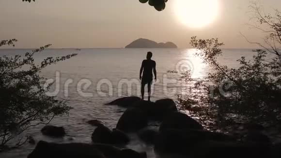 日落时一个年轻人站在海底的岩石上视频的预览图