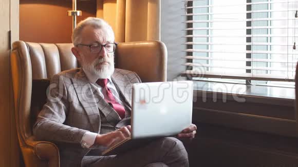 时尚的老年男性作家穿着优雅的衣服在笔记本电脑上工作视频的预览图