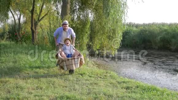 在乡下度过一个愉快的家庭假期父亲和儿子在河边的手推车里用芦苇乱逛视频的预览图