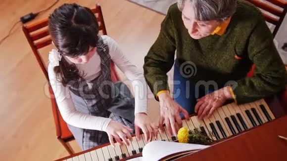 音乐课弹钢琴的女孩年长的老师坐在旁边和女孩一起弹俯视图视频的预览图