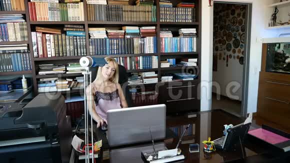 优雅开朗的女人在办公室的笔记本电脑上工作那里有很多书年轻漂亮的开朗女人视频的预览图