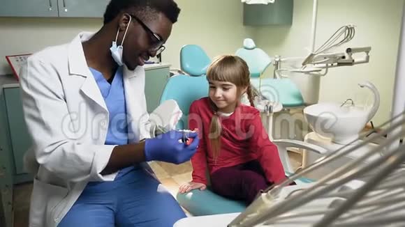 向年轻女性患者展示如何在塑料模型上刷牙的非洲牙医视频的预览图