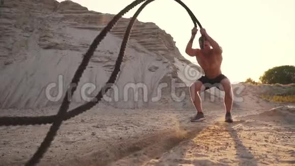 男运动员在沙滩上推UPS用绳子打地面在沙滩上阳光下循环训练视频的预览图