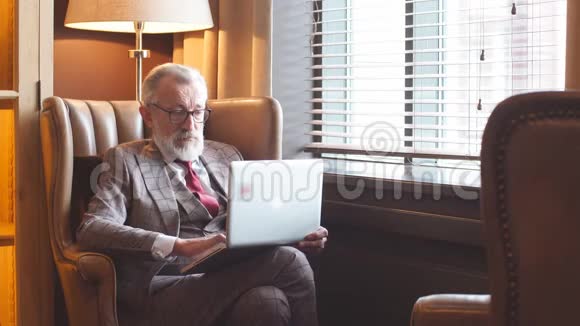 时尚的老年男性作家穿着优雅的衣服在笔记本电脑上工作视频的预览图