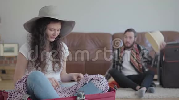 快乐的男人和女人在家里的地板上打包旅行前的手提箱妻子坐在手提箱里视频的预览图