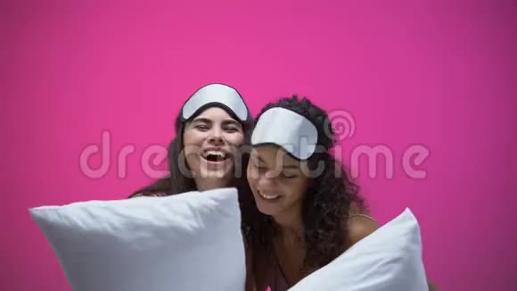 两位女士穿着睡衣戴着眼罩抱着枕头拥抱和欢笑休息视频的预览图