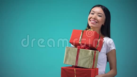 微笑的女孩手里拿着许多礼品盒节日礼物站在蓝色的背景上视频的预览图