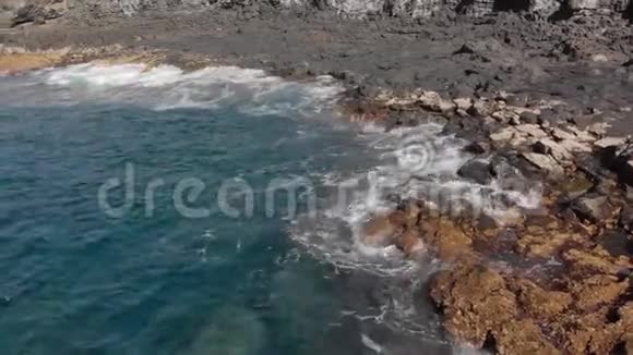 空中射击圆形的波浪在石头和干燥的火山海岸线上溅起蓝色和绿松石视频的预览图