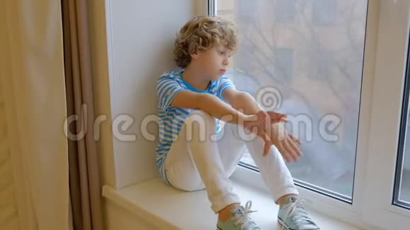 坐在窗台上的金发卷发男孩向窗外望去一个六岁的孩子独自坐在卧室里很伤心视频的预览图