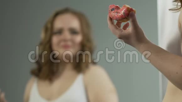 沮丧的超重女孩照镜子绝望地吃甜甜圈视频的预览图