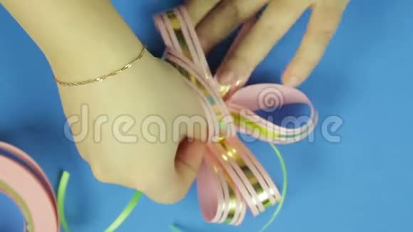 女人双手系着粉红色的辫子粉红色的空白作为礼物蝴蝶结蓝色背景视频的预览图