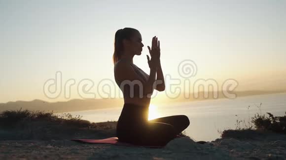 女人在垫子上练习瑜伽在日出时冥想慢动作视频的预览图