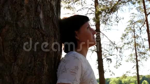 一个小女孩站在森林里的一棵树旁运动摄影机滑块在树林里休息在新鲜空气中散步视频的预览图
