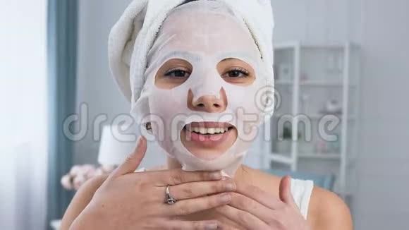 微笑的女人在脸上固定恢复活力的化妆品白色组织面具视频的预览图