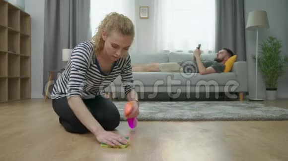 疲惫的妻子打扫地板丈夫用智能手机躺在沙发上视频的预览图