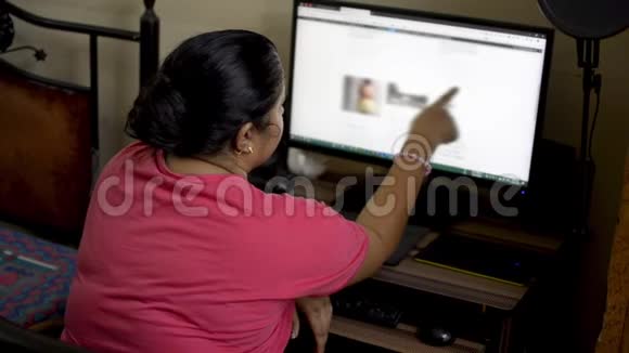 印度亚裔白种人女性穿着粉红色t恤在家中使用台式电脑妻子浏览网页视频的预览图
