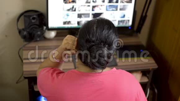 印度亚裔白种人女性穿着粉红色t恤在桌面电脑上工作手放在下巴上妻子浏览互联网博客视频的预览图