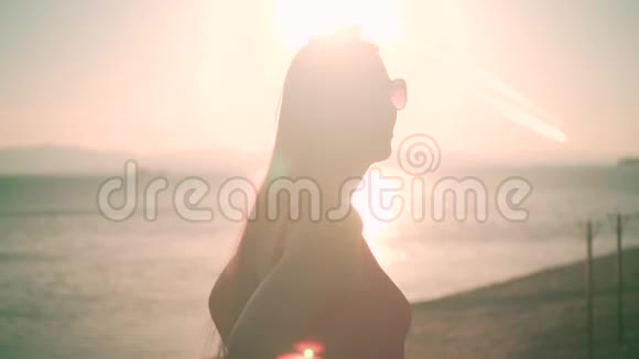 一个穿着红色的一件泳衣和眼镜的漂亮女孩站在夕阳的光线下的海滨视频的预览图
