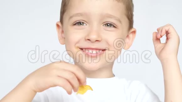 一个高兴和高兴的孩子吃薯片坐在白色背景的桌子上特写视频的预览图