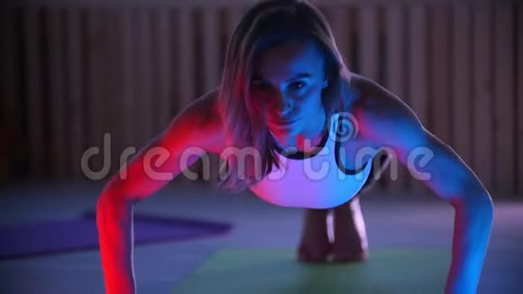 年轻女子健身教练在霓虹灯照射室做俯卧撑视频的预览图