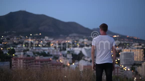 夜间在山顶举起双臂的青年游客的后景视频的预览图