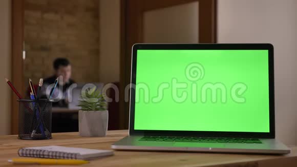 笔记本电脑绿色屏幕的特写镜头放在笔记本旁边的桌子上铅笔放在一个杯子里上面显示着一个视频的预览图