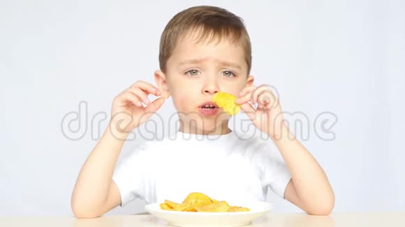 一个喜欢吃薯片的孩子坐在白色背景的桌子旁3男孩伸出手来视频的预览图