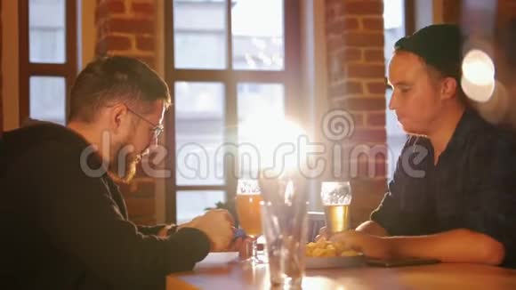 两个人坐在餐厅的桌子旁喝啤酒其中一个打电话给某人视频的预览图