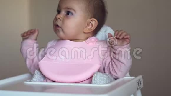 可爱的女婴坐在高椅子上的硅胶围兜用于食品概念厨房视频的预览图