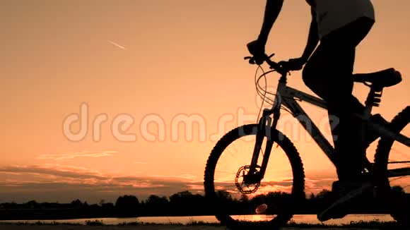 一个穿着白色T恤的少年骑着自行车在黎明的清晨骑着自行车穿过河流或湖泊一个骑自行车的人的剪影视频的预览图