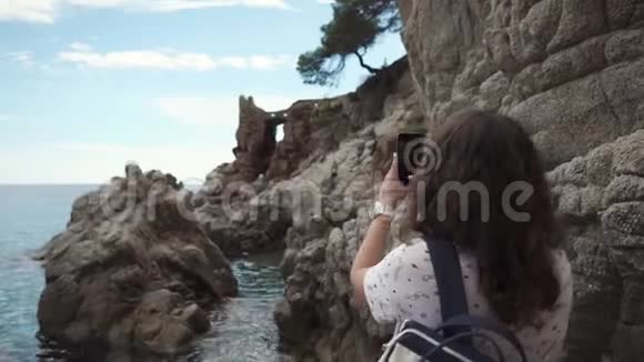 布鲁内特女士正在用手机拍摄海岸上美丽的岩石视频的预览图