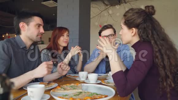 友好的男性和女性同事在咖啡馆里吃披萨在午休时一起聊天和玩视频的预览图